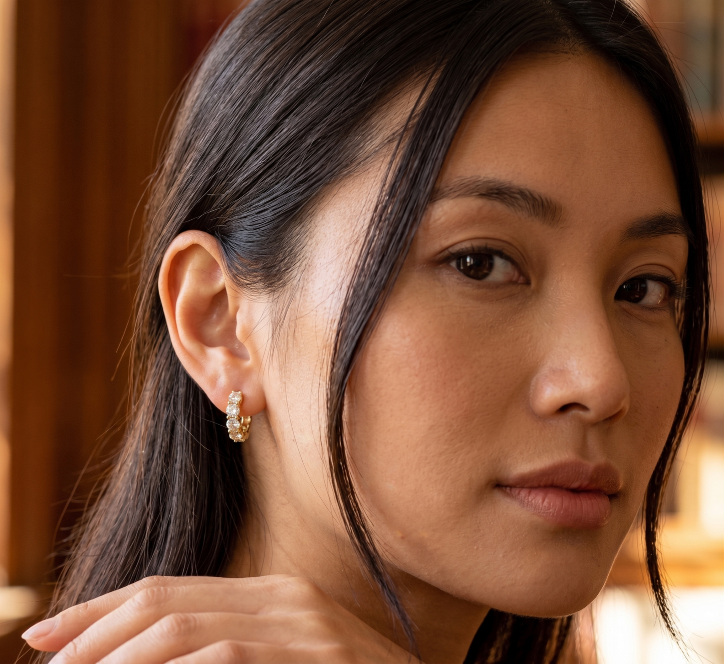 Close-up of a woman wearing gold moissanite diamond hoop earrings with a blurred background